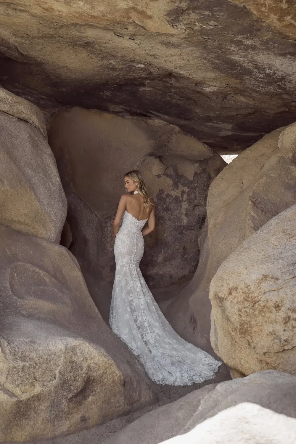 A woman in a strapless lace wedding dress stands gracefully among rocky formations.