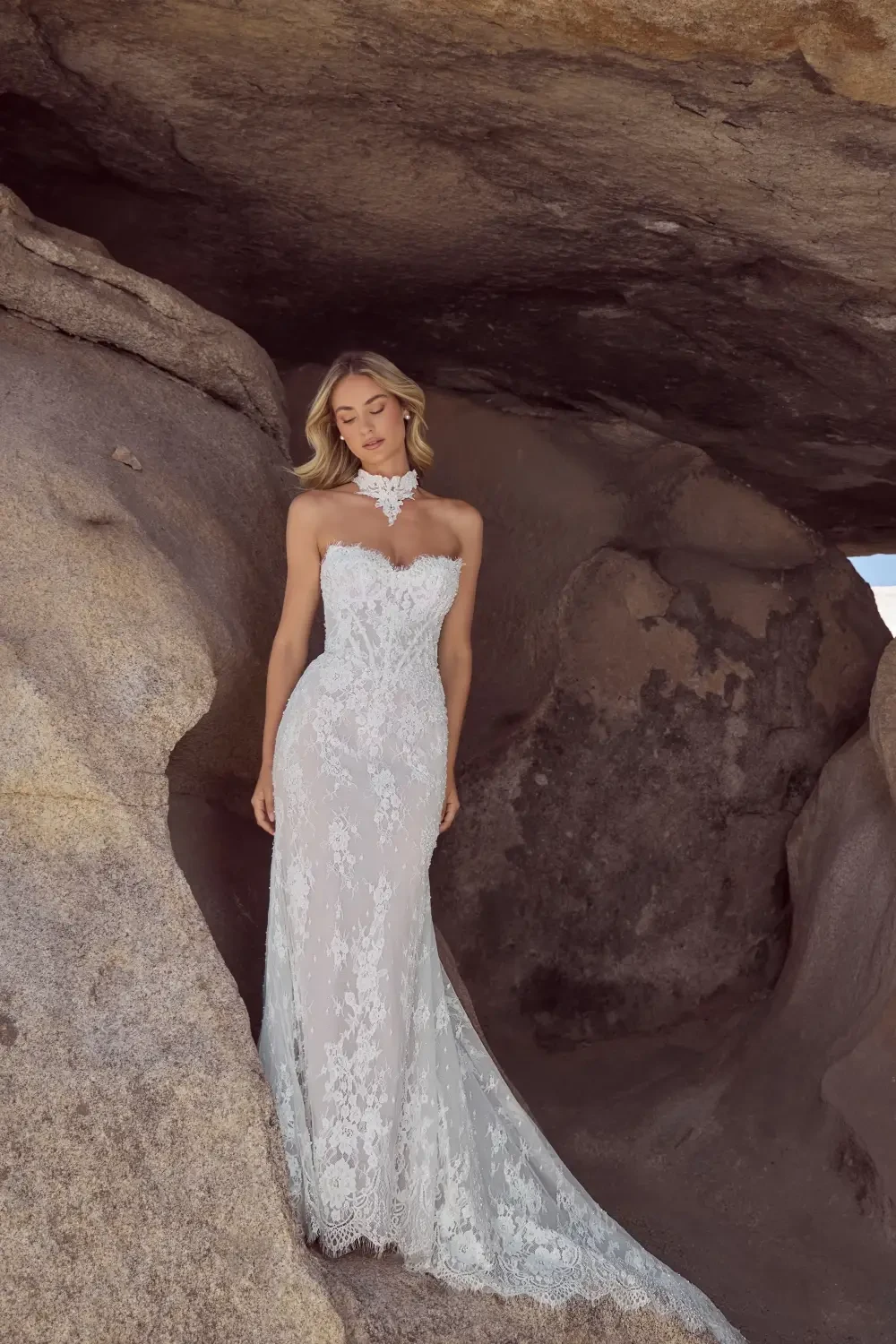 A woman in a strapless lace wedding dress stands gracefully among rocky formations.